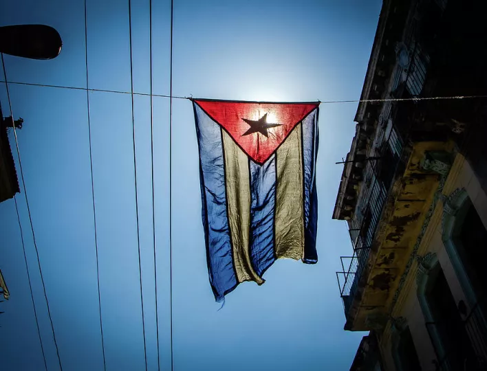 Bandera cubana ondeando en un entorno urbano, reflejando el contexto nacional de la noticia.