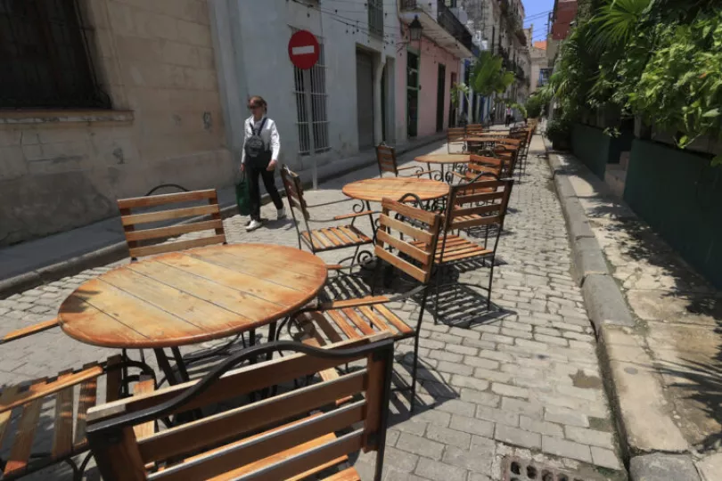 Persona caminando frente a un conjunto de mesas y sillas vacías en La Habana, reflejando el declive del turismo.