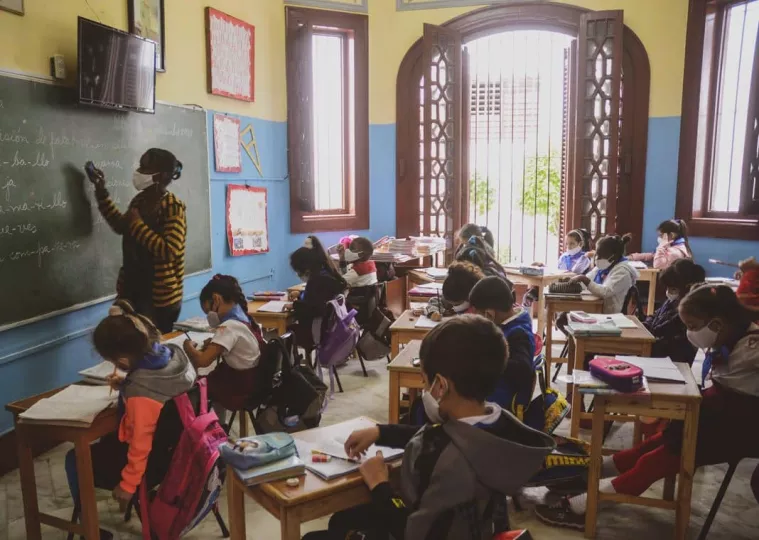 Aula de una escuela cubana con maestros frente a pupitres vacíos.