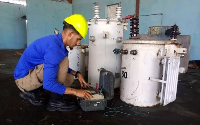Trabajador en un taller eléctrico realizando labores de mantenimiento a un transformador.