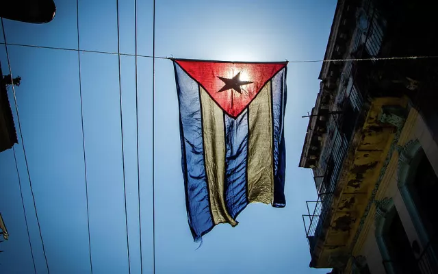 Bandera cubana ondeando en un entorno urbano, reflejando el contexto nacional de la noticia.