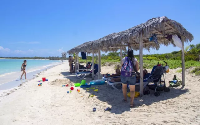 Vista panorámica de una playa cubana con estructuras de sombra y vegetación en el entorno.