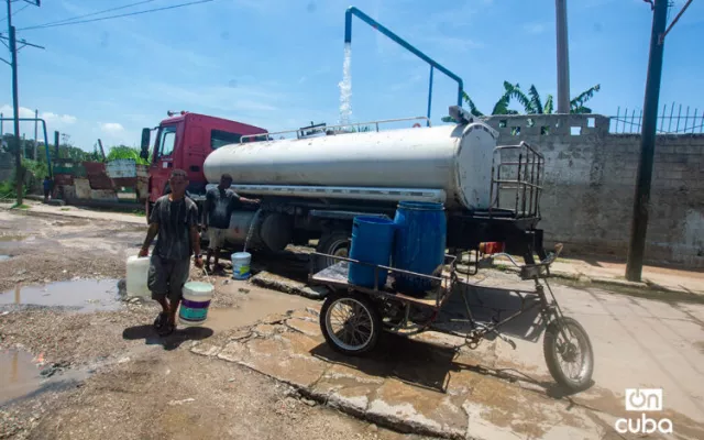 Personas llenando recipientes con agua en La Habana junto a una pipa de servicio.