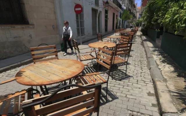 Persona caminando frente a un conjunto de mesas y sillas vacías en La Habana, reflejando el declive del turismo.
