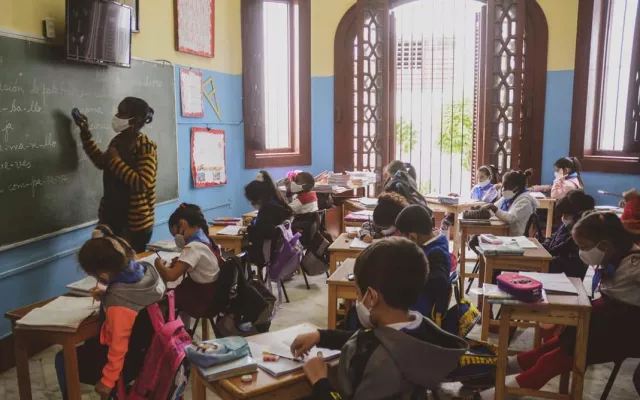 Aula de una escuela cubana con maestros frente a pupitres vacíos.